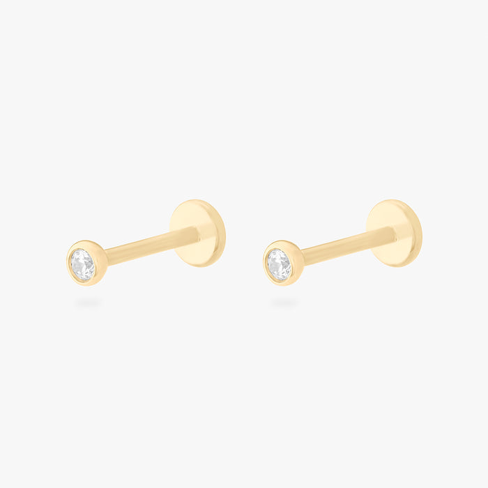 This is an image of a 14k gold flatback with a bezel setting and clear stone on ear. [pair] color:null|14k gold