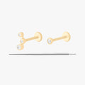 This image displays a set of two 14K gold flatback studs and a flatback insertion tool. The two earrings included in this set are the 14K Bezel Flatback Stud in gold/clear, as well as the 14K CZ Bezel Cluster Flatback Stud in gold/clear.