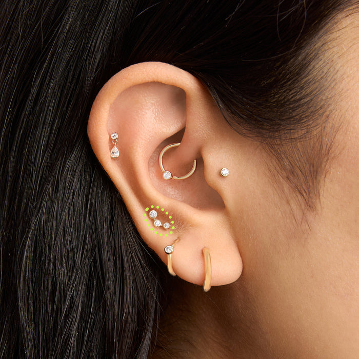 This is an image of a 14k gold flatback stud with 3 clear cz bezels in a cluster shape on ear.