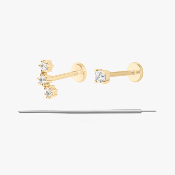 This image displays a set of two 14K gold flatback studs and a flatback insertion tool. The two earrings included in this set are the 14K Mini CZ Flatback Stud in gold/cleat, as well as the 14K Cluster Flatback Stud in gold/clear.