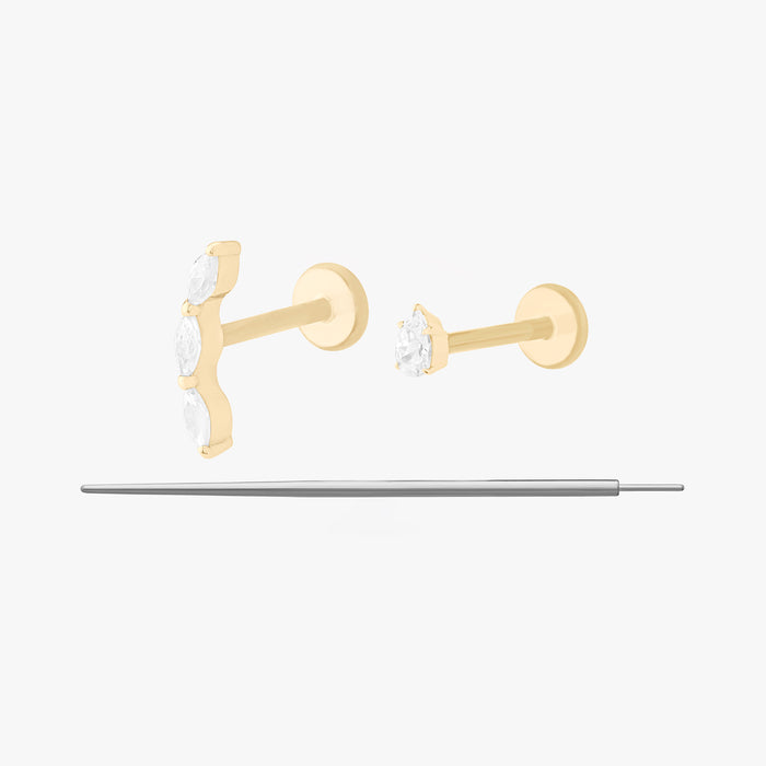 This image displays a set of two 14K gold flatback studs and a flatback insertion tool. The two earrings included in this set are the 14K Pear Clear Flatback Stud in gold/clear and 14K Curved CZ Pear Flatback Stud in gold/clear.