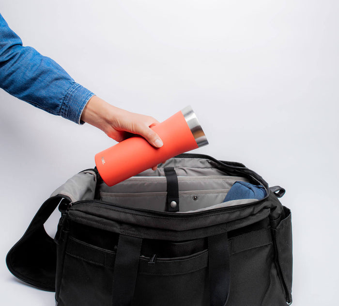 Angled view of 16oz Leakproof Travel Mug in orange showing stainless-steel rim being placed into open black duffel bag