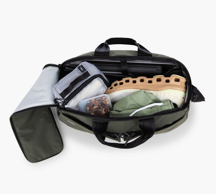 Olive-green 25L duffel open to show packed shoes, zippered packing cube, container of nuts, and folded shorts
