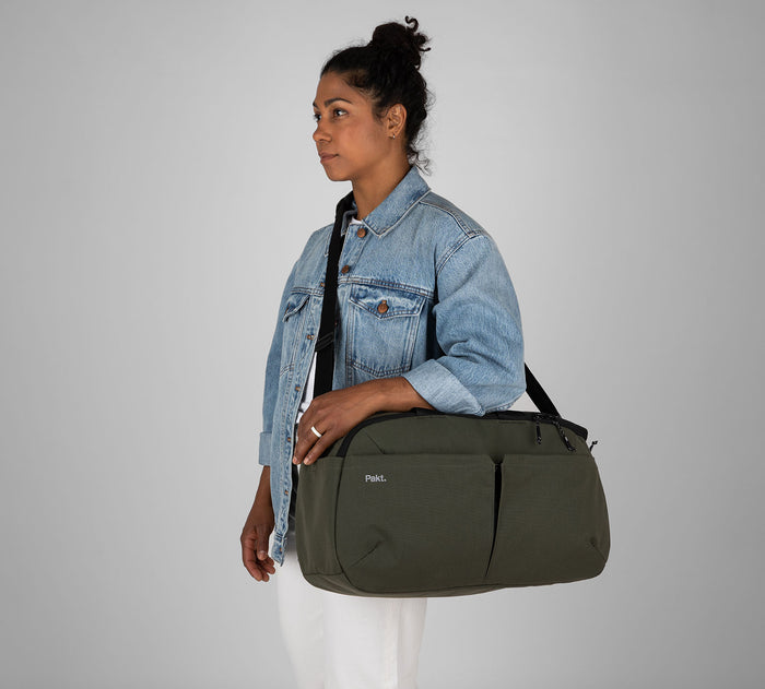 Woman wearing denim jacket carrying olive-green duffel bag with shoulder strap