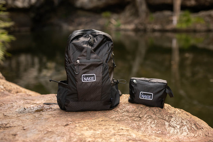 Black foldable backpack 30L with NAKIE logo, shown with matching small pouch by water