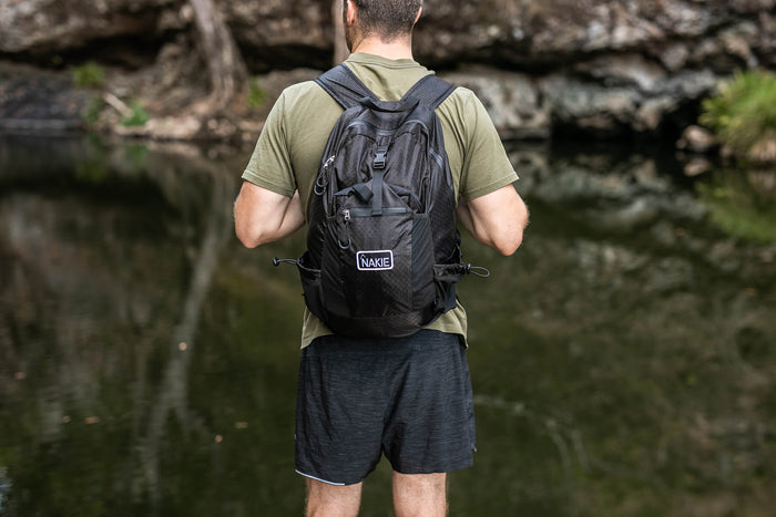 Black foldable 30L backpack with padded shoulder straps, worn on back view by man in outdoor setting