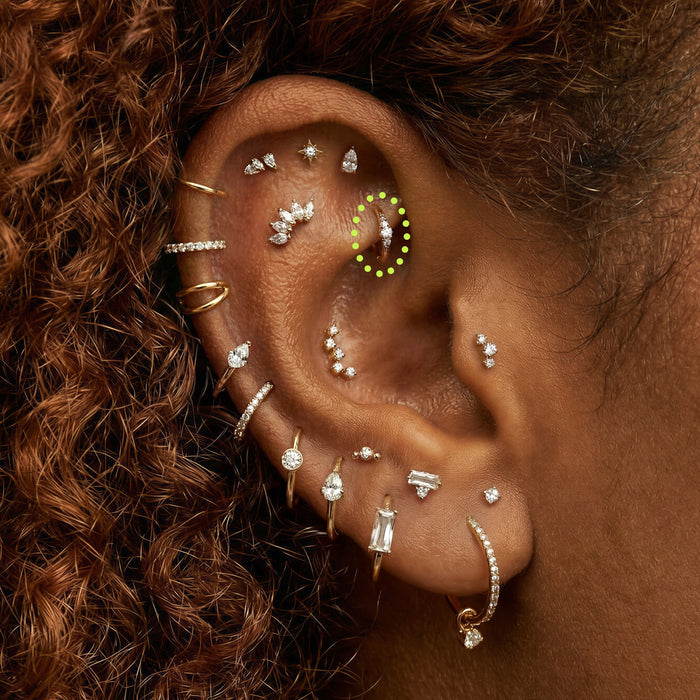 Close-up of an ear with multiple gold and stone earrings with a 5mm stacked cz gold clicker circled in the rook