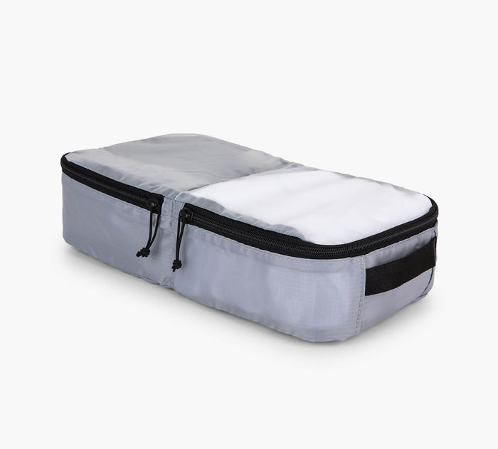 Angled view of grey packing cube showing dual zippered compartments and side carry handle on white background