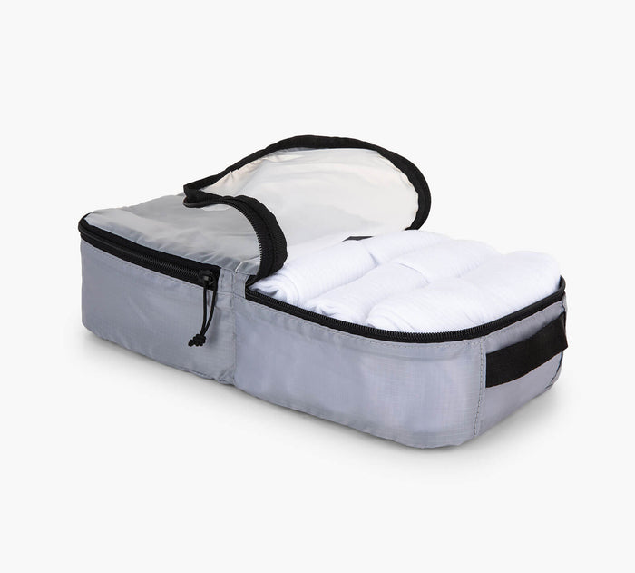 Three-quarter view of grey packing cube open to show folded clothes and interior mesh pocket on white background