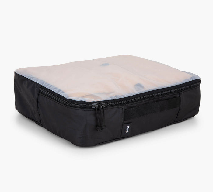 Angled front view of black packing cube showcasing translucent mesh top, zip closure, and Pakt tag on white background