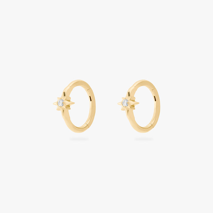 A pair of gold hoop earrings, each with a small star-shaped stone, against a white background.
