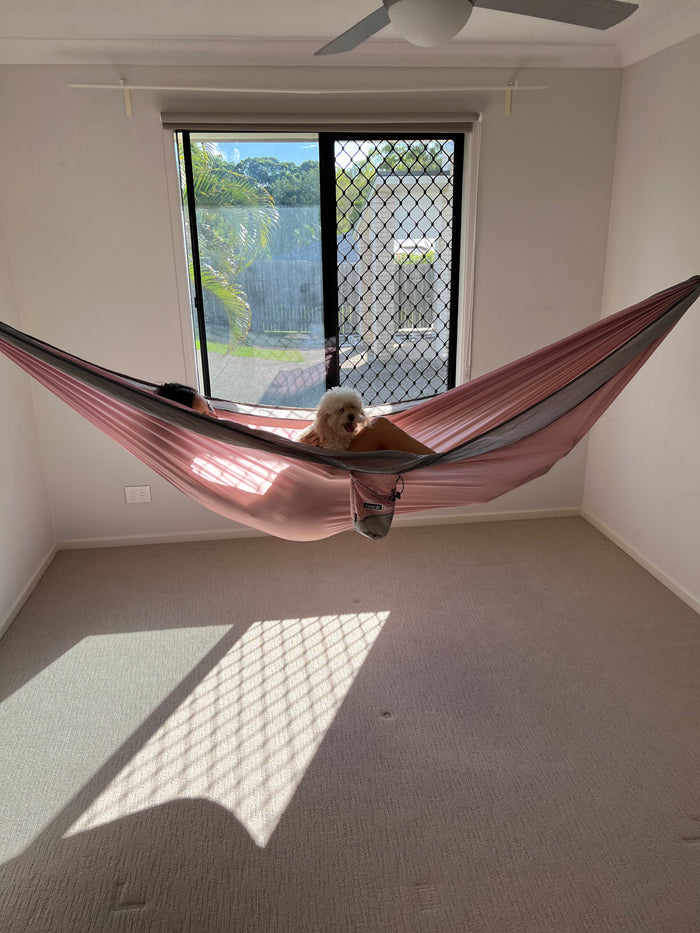 Burgundy and gray striped camping hammock strung indoors between wall anchors with person relaxed inside