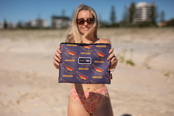Adelaide Crows navy beach towel with repeated orange text and Crows logo, held up on sand beach