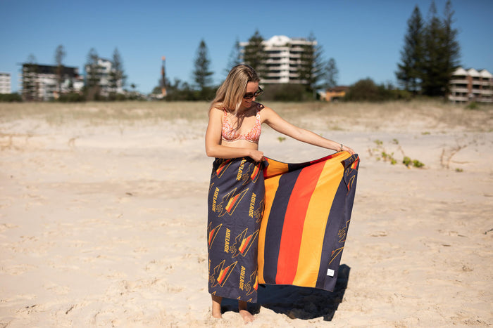 Adelaide Crows AFL recycled sand-free beach towel with navy, red, and gold stripes, displayed on beach.