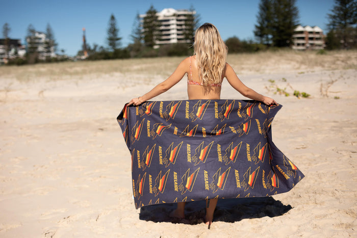 Adelaide Crows AFL recycled sand-free beach towel in navy with gold and red team logo print, displayed on beach