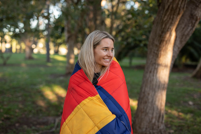 Red, gold and navy quilted puffy blanket wrapped around woman in park setting