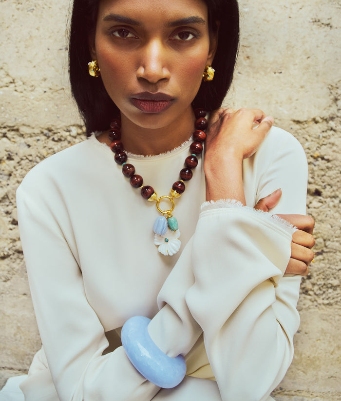 Model on tan stone wall wears white dress with Arc Cuff in Blue Lace, Desert Bloom Necklace and Kahlo hoops