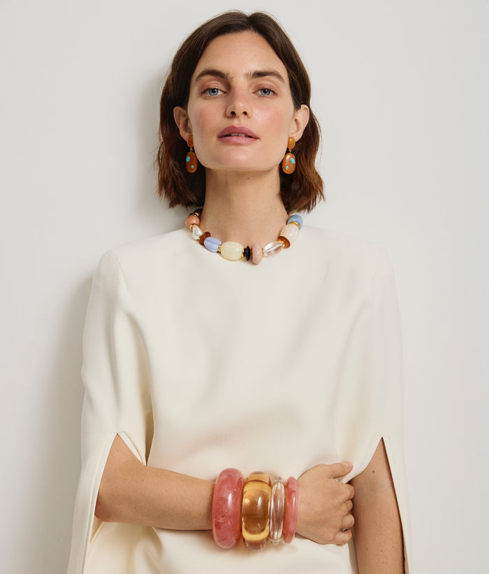 Model in white cape-dress wears stack of resin cuffs with Monument Collar and Satsuma Earrings