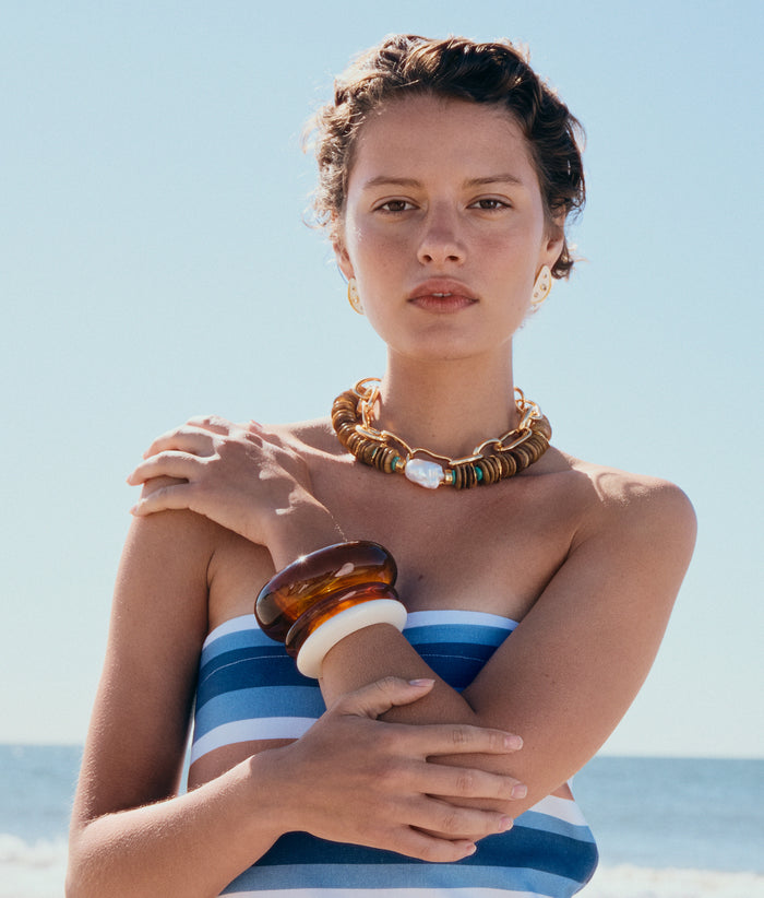 Model on beach wears striped dress with stack of resin cuffs, Kavos Collar and Porto Chain