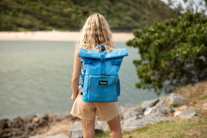 Arctic Blue recycled cooler backpack with rolled top closure, worn by person at beach overlooking water.