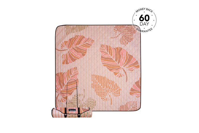 Recycled picnic blanket with autumn leaf print in coral and orange tones, shown rolled with carrying strap