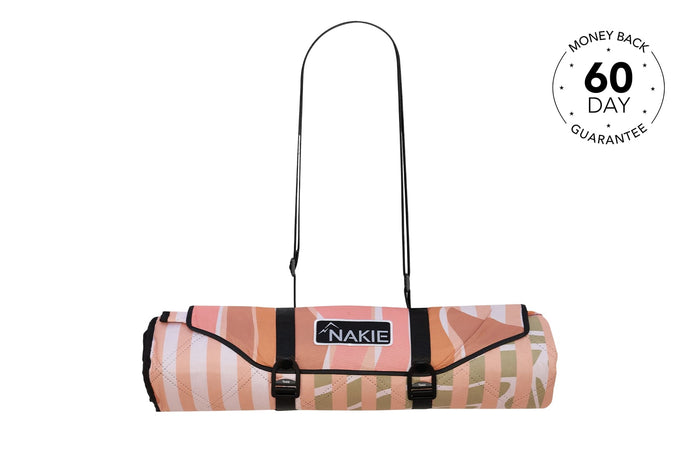 Rolled recycled picnic blanket in coral and tan geometric pattern with black carry straps and Nakie logo label.