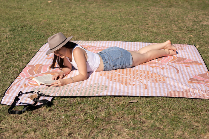 Woman wearing a hat, basking in the sun on a Nakie picnic blanket, capturing the essence of outdoor relaxation and leisure.