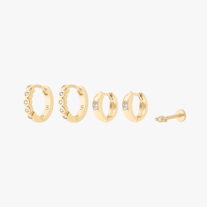 This is an image displaying the gold/clear version of the Bezel Starter Set. The set includes a pair of CZ Bezel Huggies, a pair of Chunky Pear CZ Huggies, and a single Micro Bezel Cluster Flatback Stud.