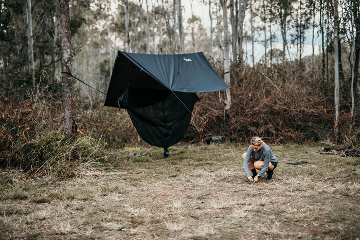 Woman setting up a Nakie ultralight no knot tarp at a campsite