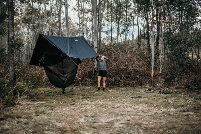 Woman effortlessly setting up a Nakie ultralight no knot tarp at a campsite