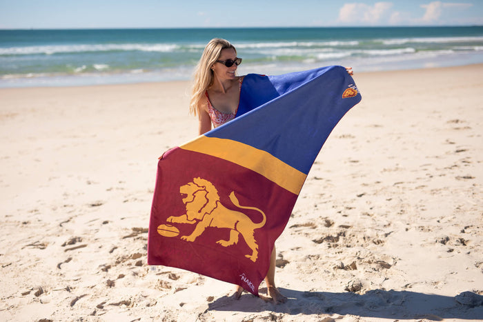 Brisbane Lions beach towel with navy, gold and burgundy color-blocking and gold lion emblem, held by woman on sandy beach