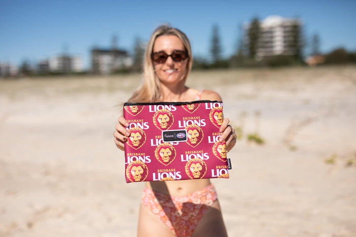 Brisbane Lions maroon beach towel with repeated lion head and text logos, held up on sandy beach