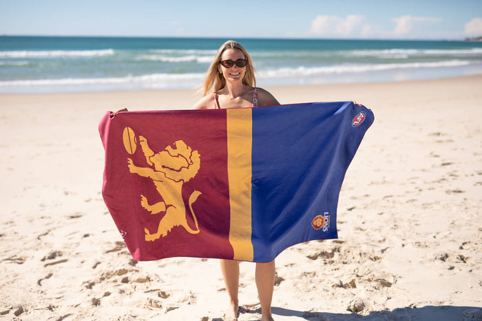 Brisbane Lions recycled sand-free beach towel in maroon, gold, and blue with lion emblem, displayed on beach.