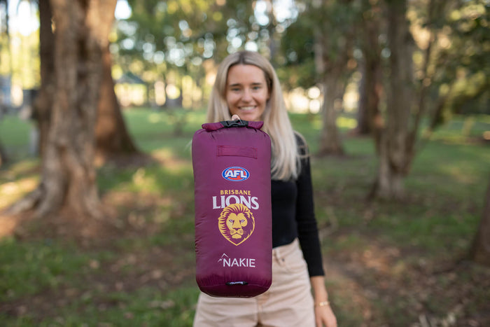 Maroon Brisbane Lions AFL puffy blanket with lion logo and Nakie branding, held up outdoors