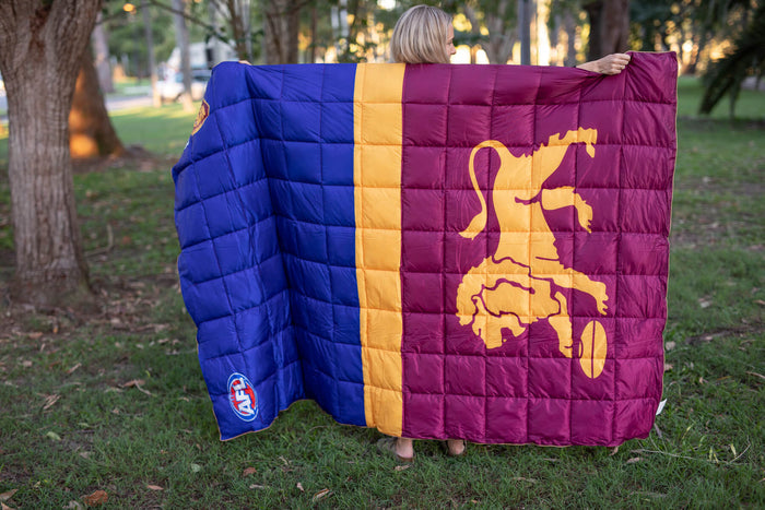 Quilted puffy blanket in blue, gold, and maroon with Brisbane Lions logo and map design, displayed outdoors.