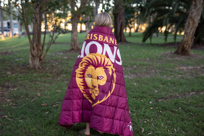 Brisbane Lions maroon puffy blanket with gold lion logo and team text, worn over shoulders outdoors