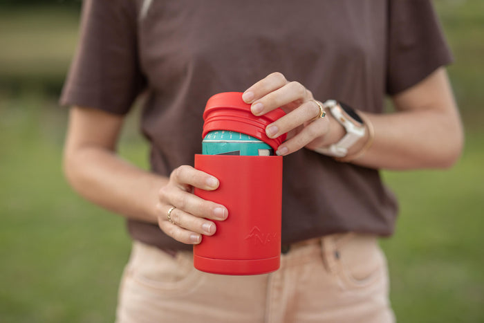 Red insulated coffee cup lid with turquoise band, held in hands outdoors