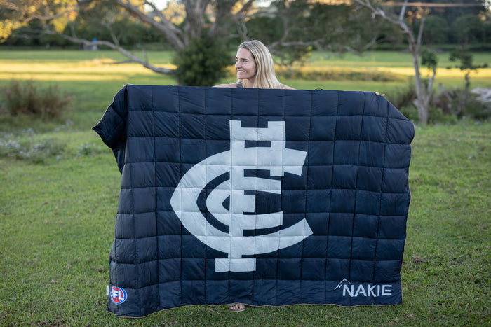 Black quilted puffy blanket with Carlton Blues AFL logo in white, held outdoors in park setting