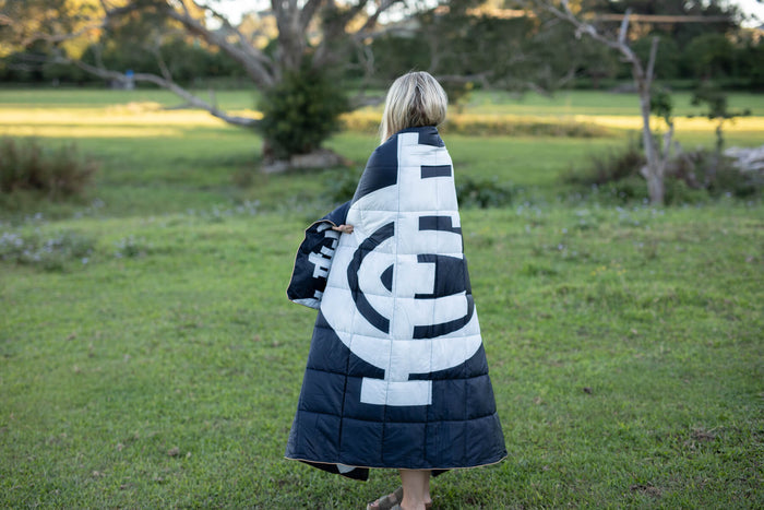 Black and white quilted puffy blanket with Carlton Blues AFL geometric design, worn draped over shoulders outdoors