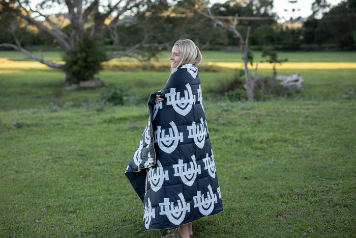 Black and white geometric patterned puffy blanket draped over woman's shoulders outdoors, showing quilted texture and all-ove
