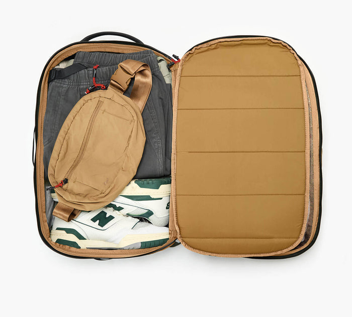 Open view of Cero Travel Backpack showcasing tan interior packed with a tan sling, gray pants, and white sneakers