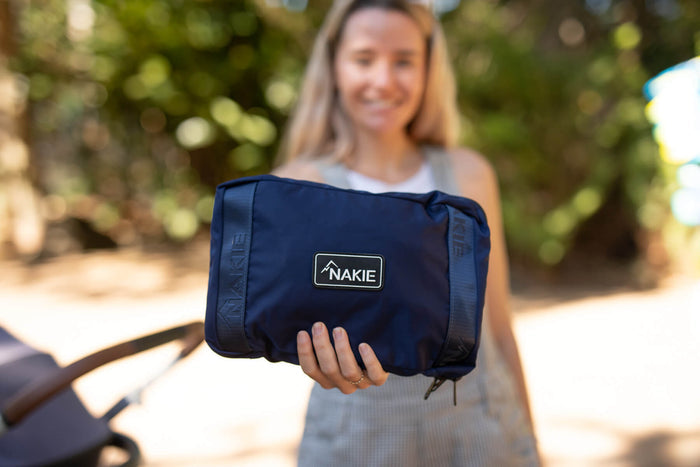 Navy recycled tote bag with NAKIE logo patch, held in hand outdoors