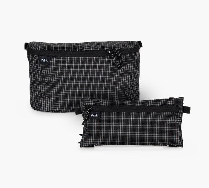 Front view of two clip-in pouches, one large 3D and one smaller flat, in black grid ripstop with top zippers and visible Pakt logo on white background