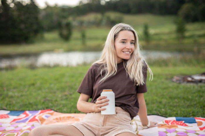 Woman holding white can cooler with orange band on picnic blanket by water