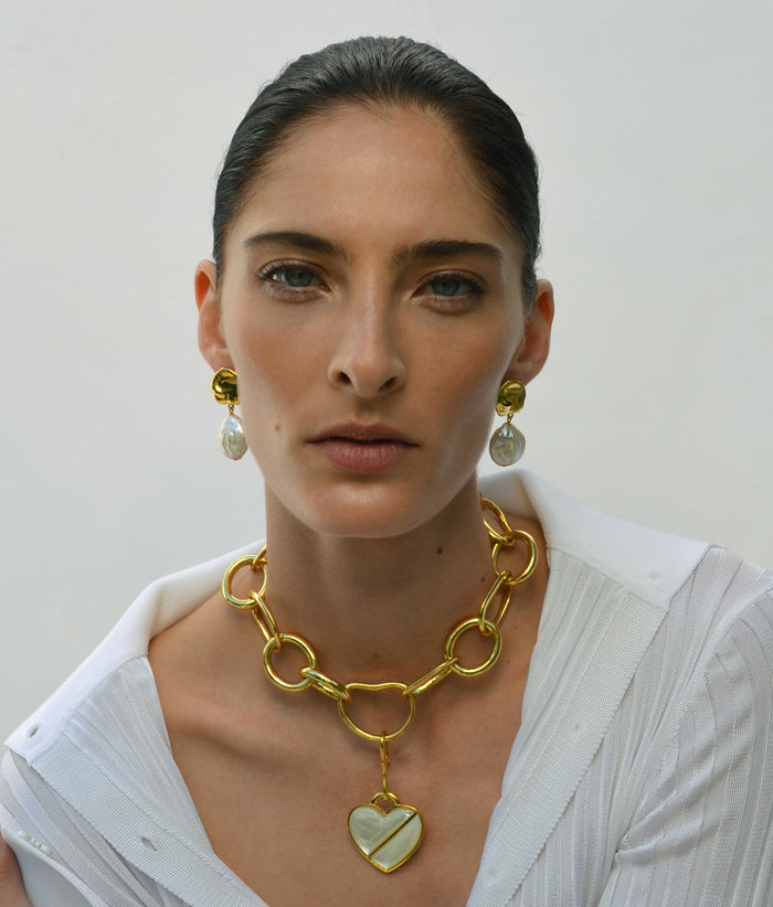 Model on grey backdrop wears white blouse with Porto Chain and heart charm and Coin Reflection Earrings