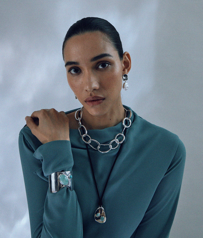 Model in teal top wears Coin Reflection Earrings in Silver with silver necklaces and bracelet.