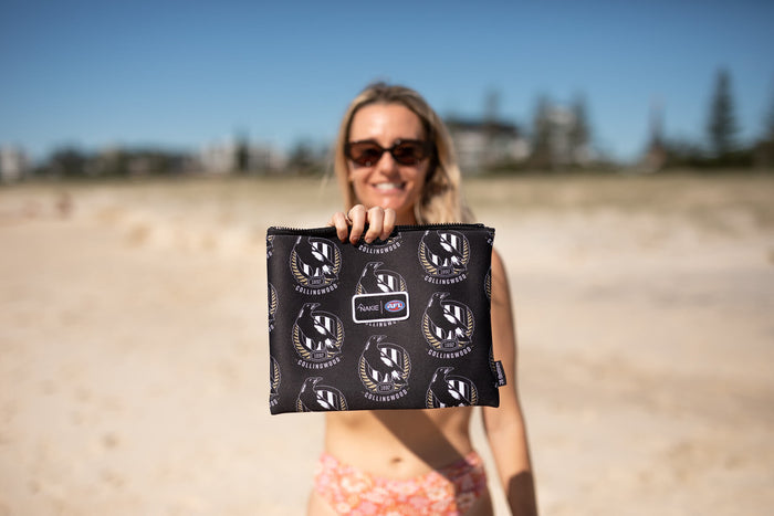 Black Collingwood Magpies AFL recycled sand-free beach towel with eagle logo pattern, held up on beach