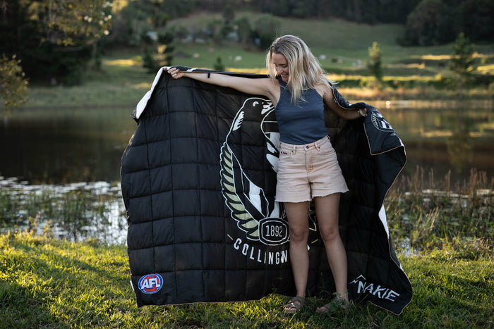 Black quilted down blanket with Collingwood Magpies AFL logo and wings emblem, displayed outdoors by water