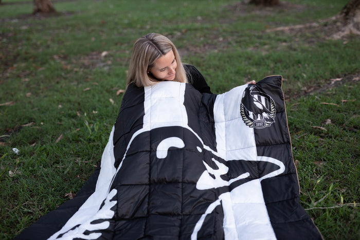 Black and white quilted down blanket with Collingwood Magpies logo and 1892 emblem, displayed outdoors on grass.