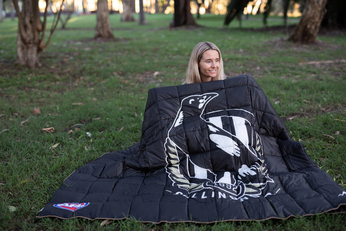 Black quilted down puffy blanket with Collingwood Magpies AFL logo and white graphic design, displayed outdoors on grass.